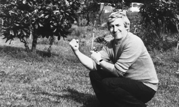 A smiling Georgi Markov sitting on a lawn in front of some bushes.